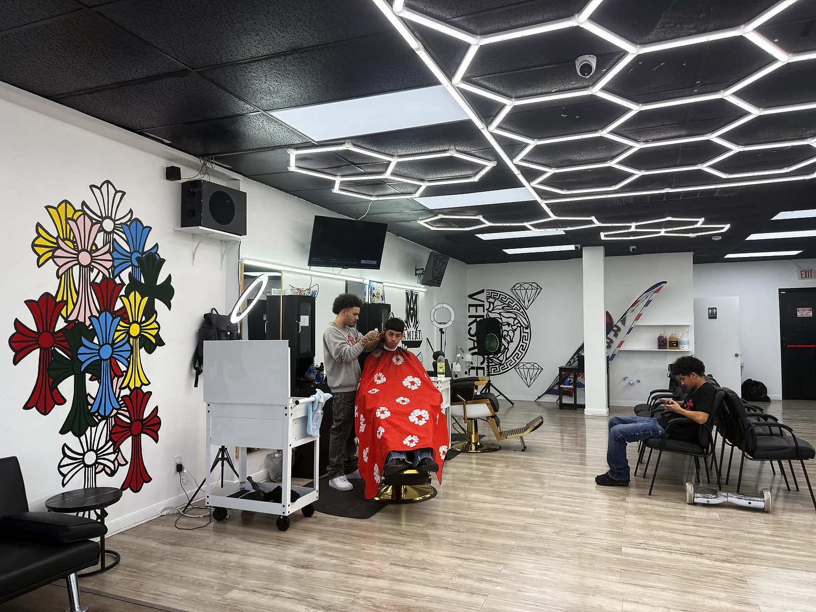 Bankz BarberHouse interior — Chrome Hearts wall, hexagon lights, gold chairs